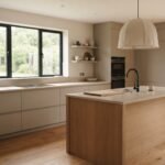 Warm minimalist kitchen with handleless greige cabinets, a light oak island, and clear stone countertops in soft morning light