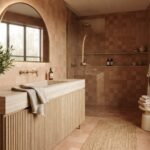 Warm terracotta tile-drenched bathroom with fluted white oak vanity, brass fixtures and arched backlit mirror — 2026 bathroom trends