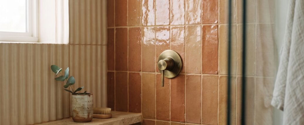 Handmade zellige shower tile in warm clay glaze with stacked vertical layout and brass fixture — bathroom tile trends 2026