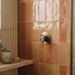 Handmade zellige shower tile in warm clay glaze with stacked vertical layout and brass fixture — bathroom tile trends 2026