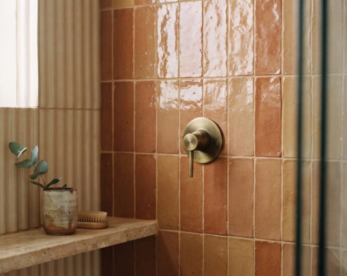 Handmade zellige shower tile in warm clay glaze with stacked vertical layout and brass fixture — bathroom tile trends 2026