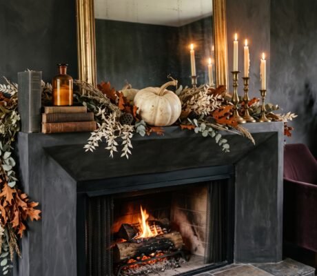 Elegant Halloween mantel decor with an asymmetric dried garland, brass candlesticks with cream tapers and a pale heirloom pumpkin