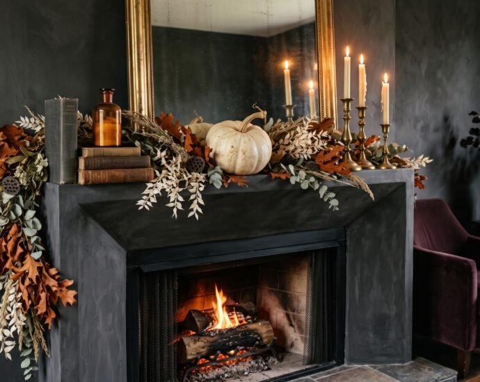 Elegant Halloween mantel decor with an asymmetric dried garland, brass candlesticks with cream tapers and a pale heirloom pumpkin