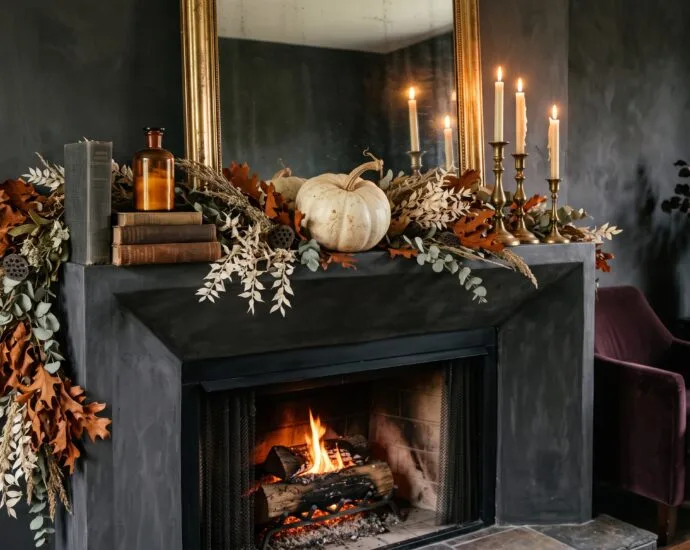 Elegant Halloween mantel decor with an asymmetric dried garland, brass candlesticks with cream tapers and a pale heirloom pumpkin